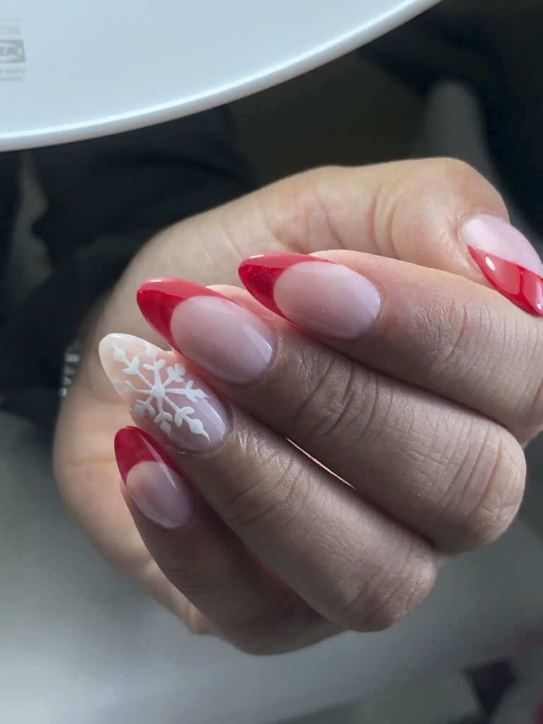 Ejemplo de tratamiento de manicura Nail Art. Uñas con la punta roja y una con dibujo de un copo de nieve